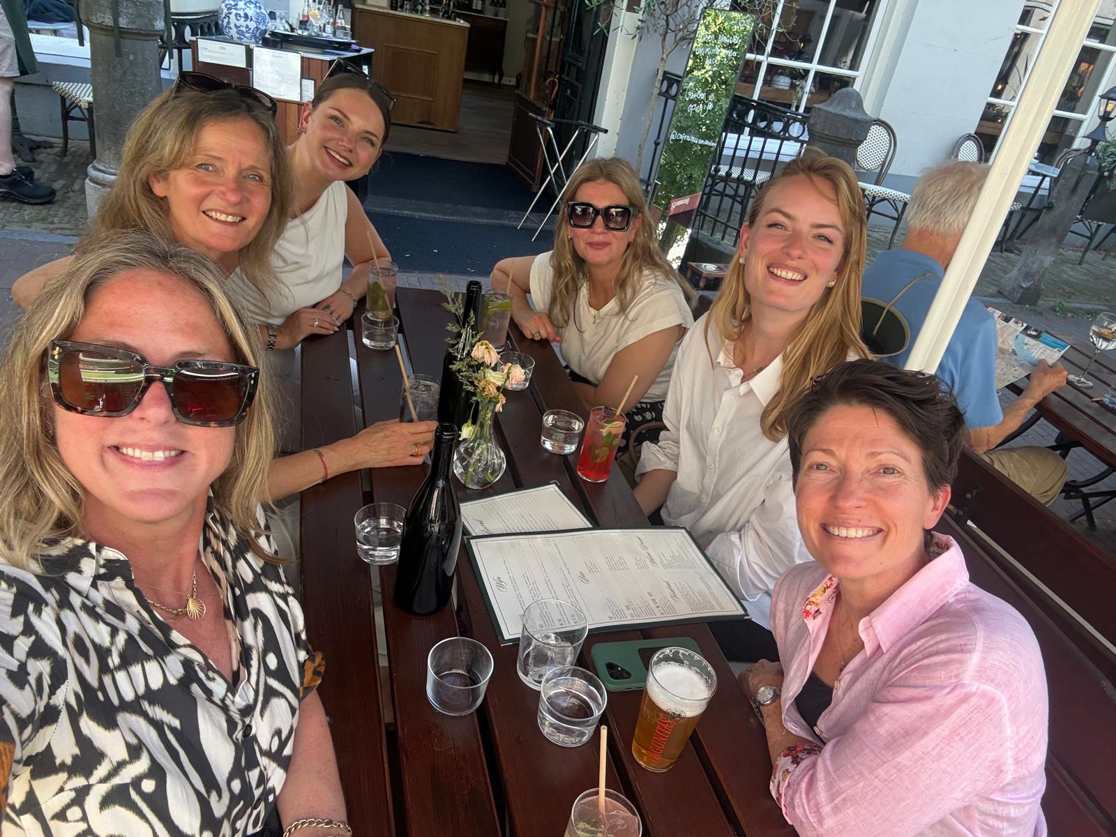 Six women smiling around an outdoor cafe table during a training break