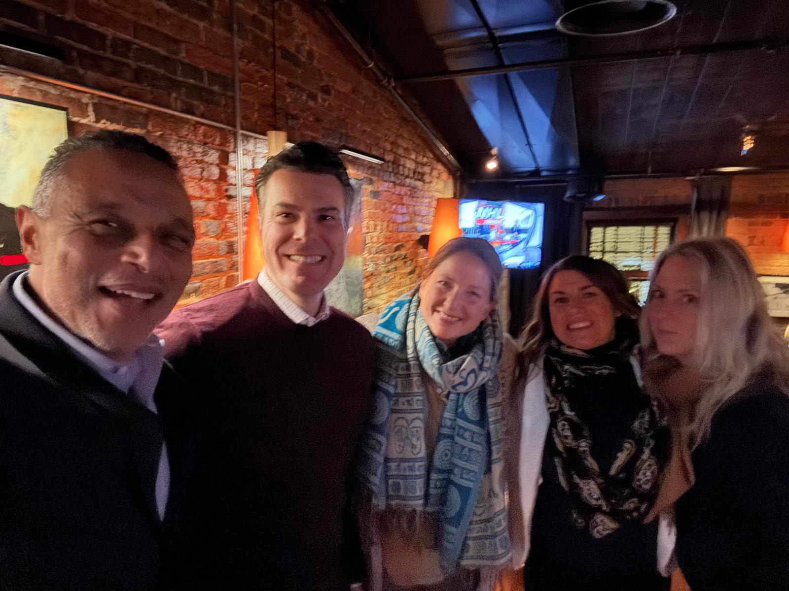 Four people smiling in front of a brick wall with art