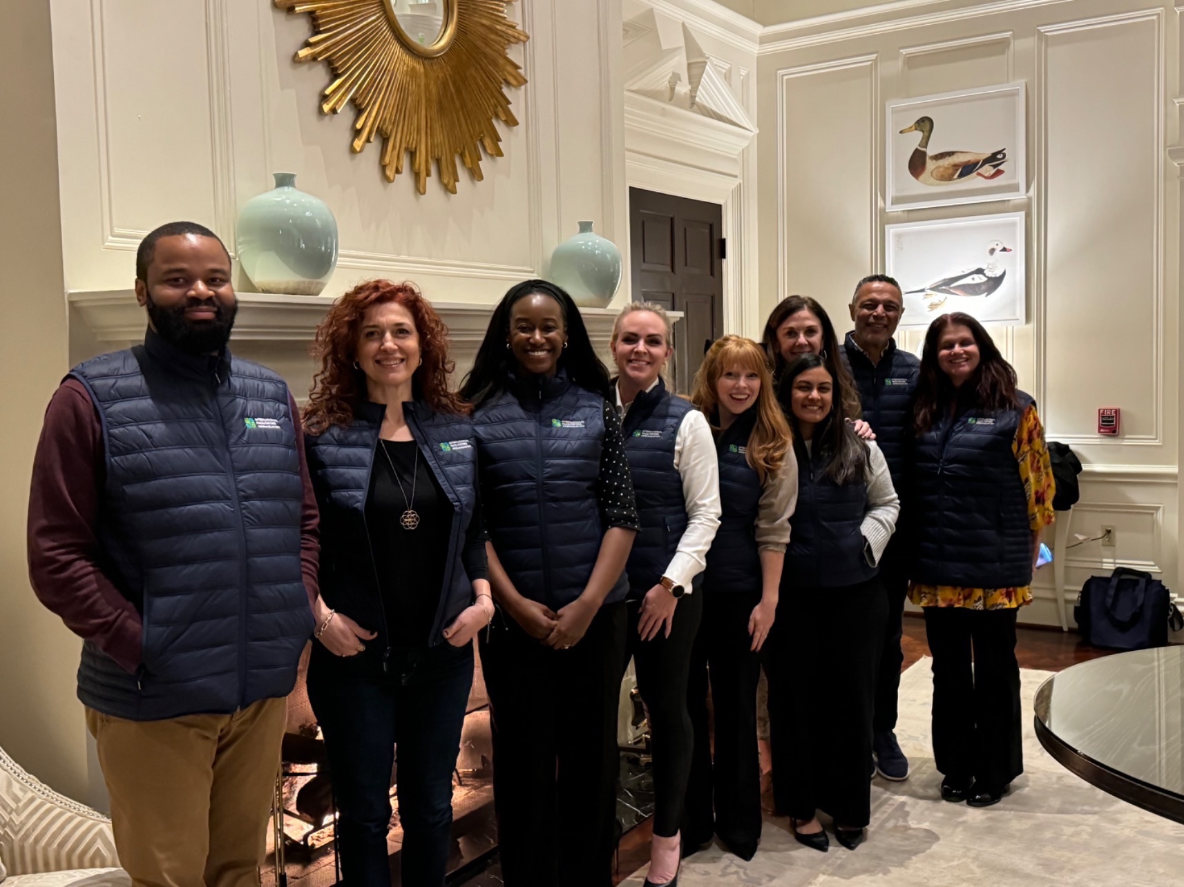 Nine people posing in a hotel conference room